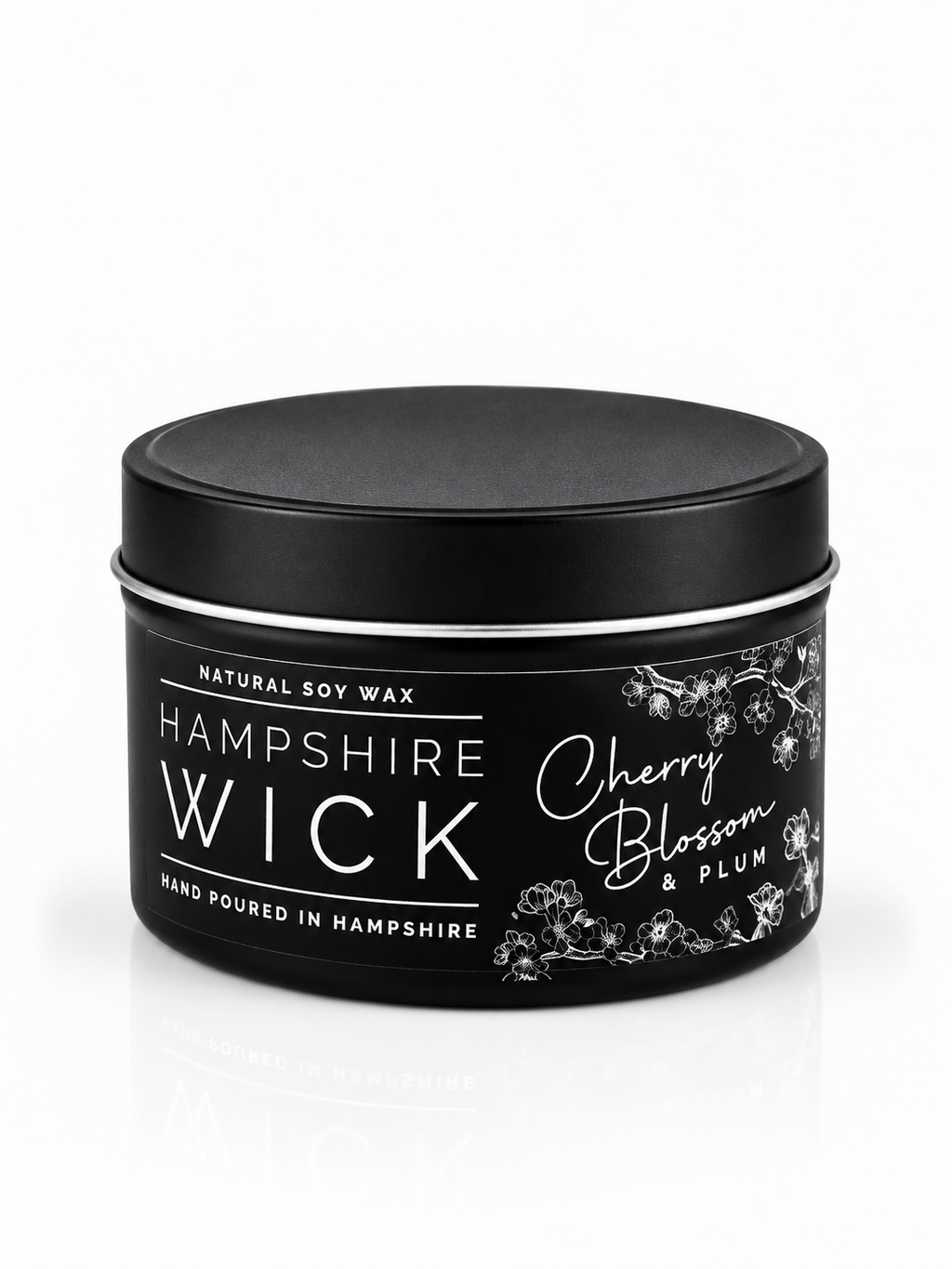 A black tin of Hampshire Wick natural soy wax candle in the Cherry Blossom & Plum scent, shown on a clean white background with a subtle reflection.