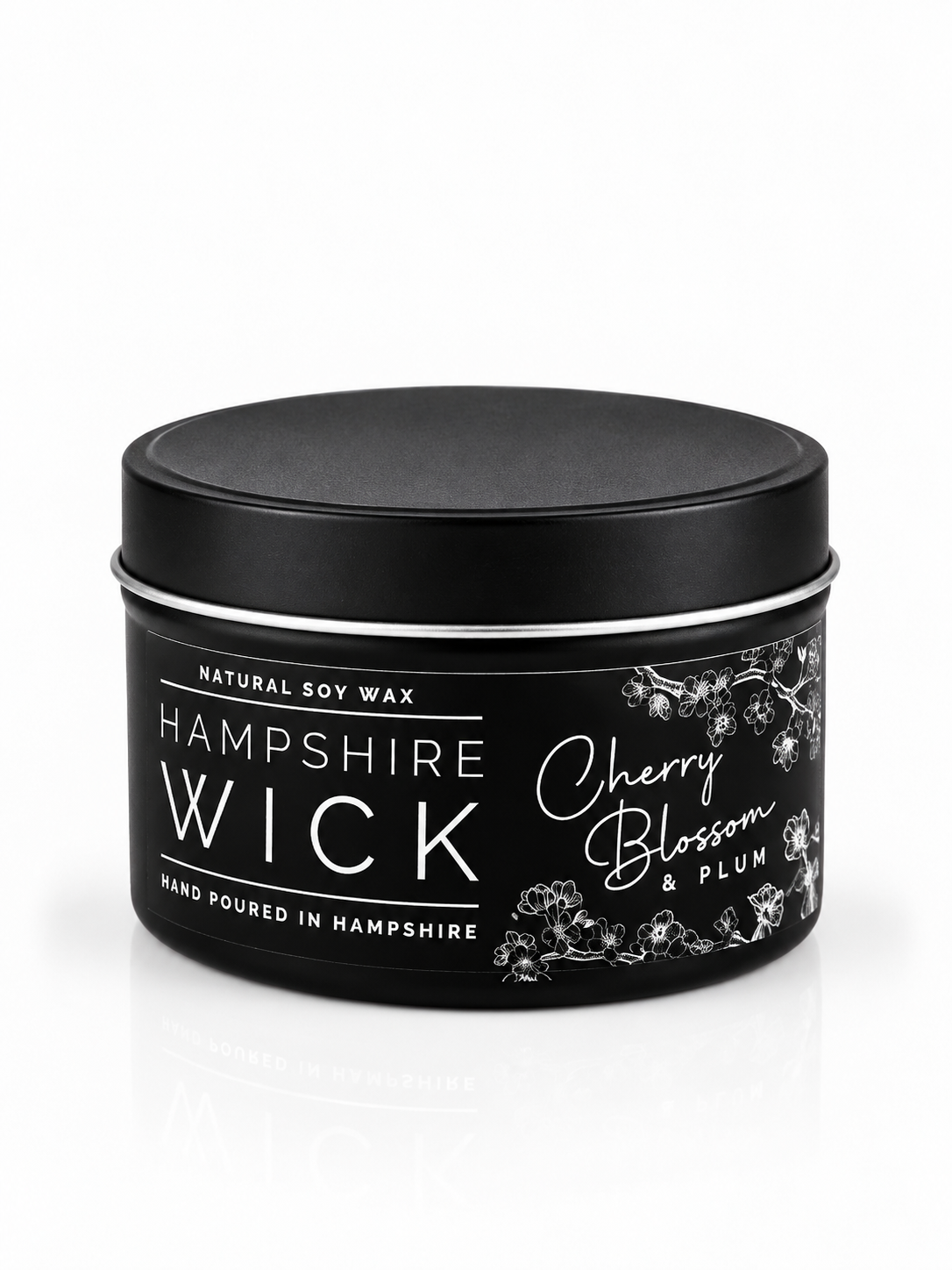 A black tin of Hampshire Wick natural soy wax candle in the Cherry Blossom & Plum scent, shown on a clean white background with a subtle reflection.